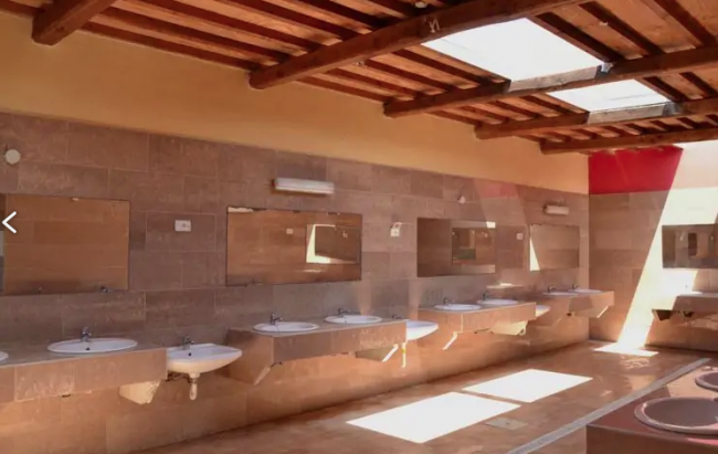 Bagni pubblici con diverse lavandini e specchi, sotto un soffitto con travi in legno e lucernari.