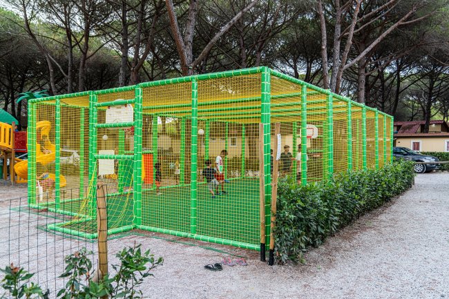 Un campo da gioco recintato con rete verde in un'area alberata.