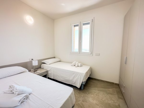 Camera con due letti singoli, comodino, finestra e ampio armadio.