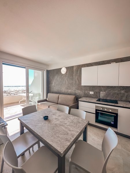 Cucina-soggiorno con tavolo, sedie, divano, cucina moderna e accesso al balcone.