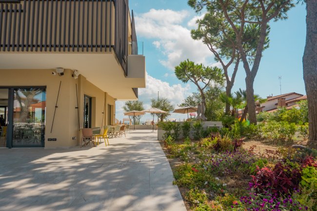 Terrazza di un edificio moderno con giardino fiorito e vista su ombrelloni da spiaggia.