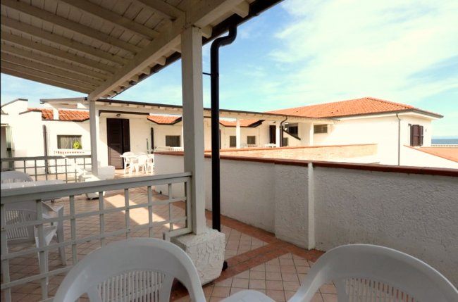 Terrazza coperta con sedie bianche, vista su edifici bianchi e mare.