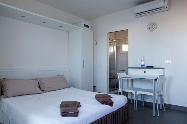 Camera da letto moderna con letto matrimoniale, tavolo, due sedie e bagno annesso.