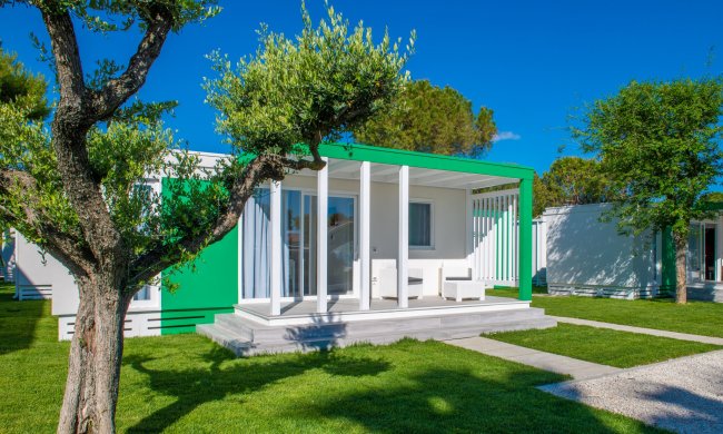 Bungalow moderno bianco e verde circondato da prato e alberi.
