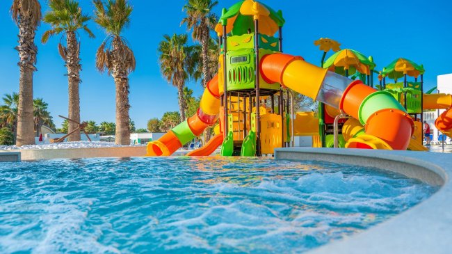 Un parco acquatico con scivoli colorati e palme sullo sfondo.