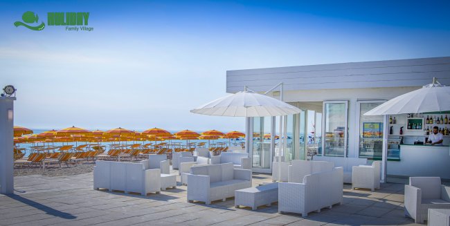 Bar all'aperto con sedute bianche e ombrelloni, vista mare.