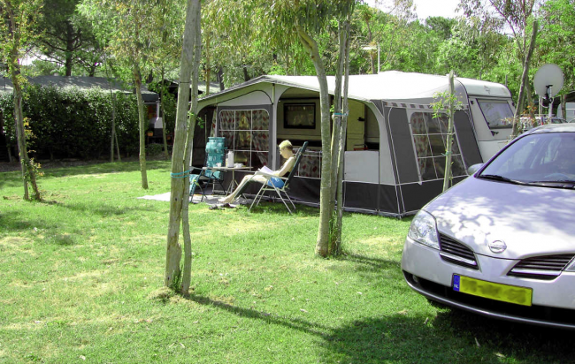 Tenda da campeggio con persona seduta fuori e un'auto parcheggiata.