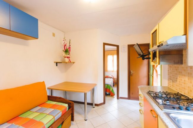 Cucina con divano arancione, tavolo, ingresso di una camera e piano cottura.