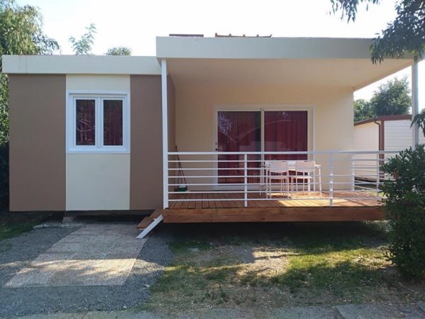 Casetta beige con terrazza e ringhiera bianca, circondata dal verde.