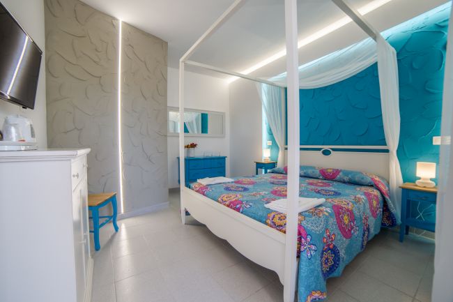 Camera da letto con letto a baldacchino colorato, mobili bianchi e tocchi di blu.
