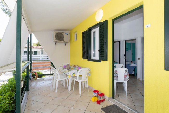 Veranda gialla con tavolo rotondo e sedie bianche, affaccio su un giardino.