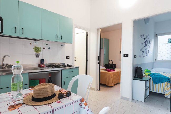 Interno con cucina verde acqua, tavolo apparecchiato, e due camere da letto adiacenti.