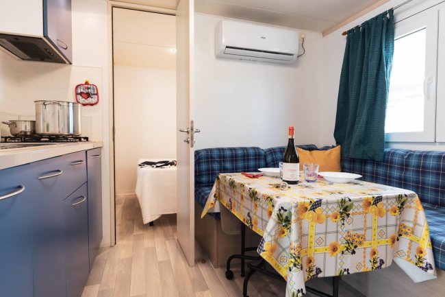 Interno di un bungalow con tavolo apparecchiato, divano a quadri e cucina.