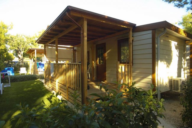 Veranda di legno di un bungalow con giardino verde intorno.