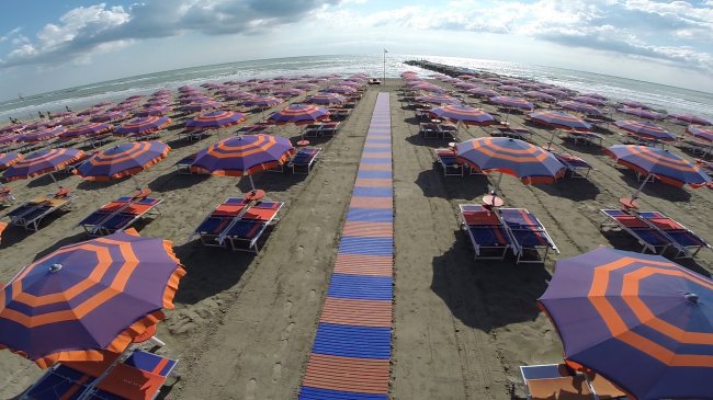 Spiaggia con file ordinate di ombrelloni e lettini colorati.