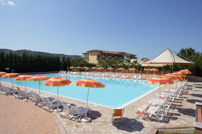 Ampia piscina con ombrelloni gialli e arancioni. Lettini disposti ordinatamente intorno.