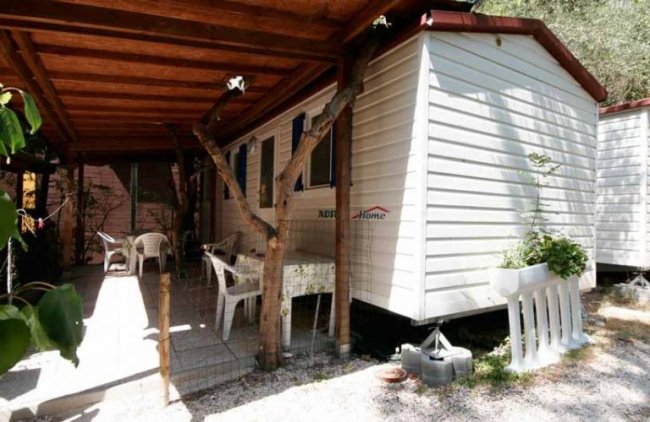 Mobile home con veranda coperta e sedie bianche.