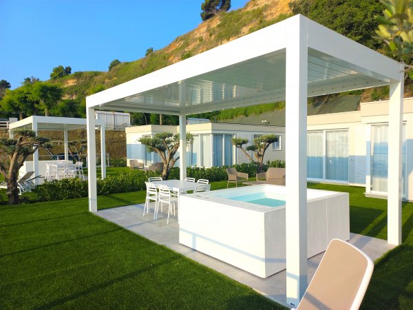 Patio moderno con tavolino e sedie, circondato da verde.