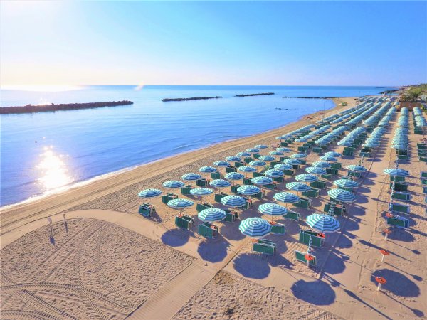 Spiaggia con file ordinate di ombrelloni verdi e bianchi vicino al mare calmo.
