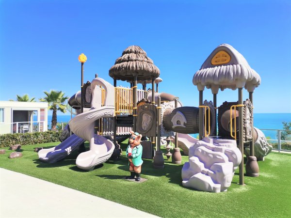 Struttura da gioco con scivoli a forma di funghi e personaggio al centro, con vista sull'oceano.