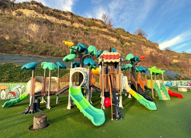 Un parco giochi con scivoli verdi sotto una collina erbosa.