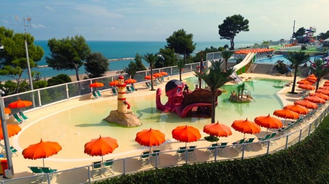 Piscina con decorazioni a tema pirata, ombrelloni arancioni e vista sul mare.