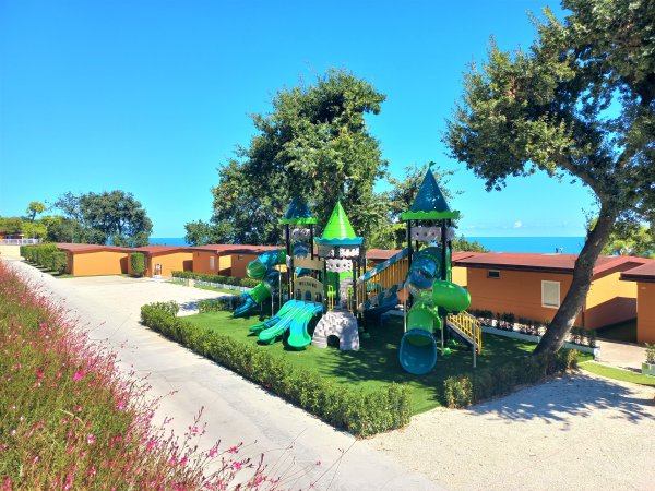 Parco giochi per bambini con scivoli verdi e torri a forma di castello.