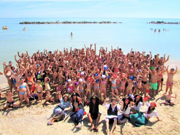 Un gruppo di persone in spiaggia esulta insieme davanti al mare.