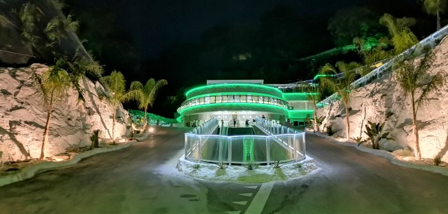 Edificio moderno illuminato di verde di notte, situato tra rocce e palme.
