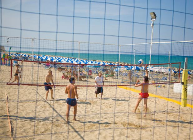 Persone giocano a beach volley sulla sabbia con il mare sullo sfondo.