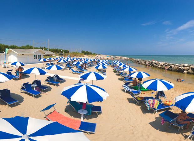 Spiaggia con ombrelloni blu e bianchi e lettini, vicino al mare con cielo sereno.