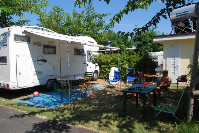 Camper parcheggiato accanto a un'area picnic con tavoli e sedie all'aperto.