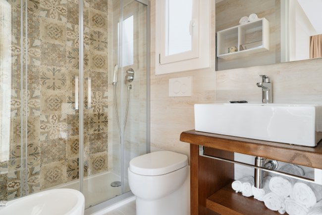 Un bagno moderno con doccia, lavabo su mobile in legno e asciugamani arrotolati sugli scaffali.