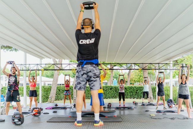 Lezione di fitness all'aperto con istruttore e partecipanti sotto un tendone.