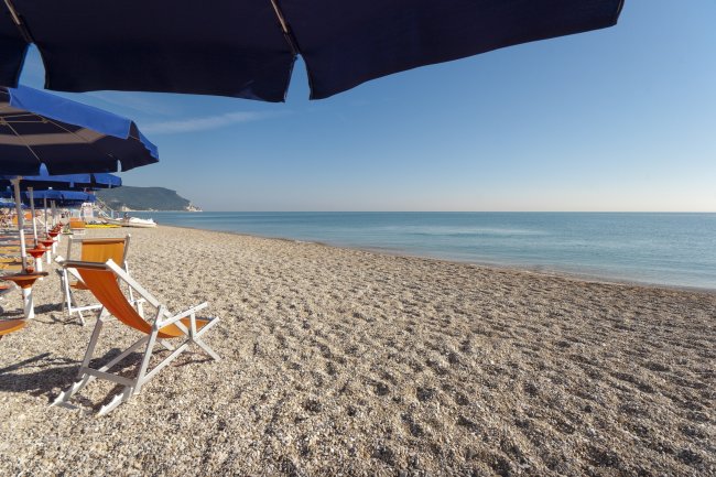 Spiaggia con ombrelloni blu e sdraio arancioni, vista sul mare calmo sotto un cielo sereno.
