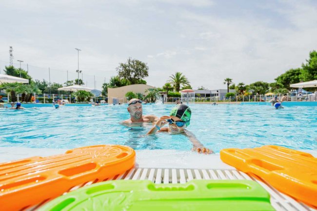 Due persone che nuotano in piscina, con palette colorate in primo piano.