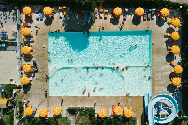 Piscina vista dall'alto con bagnanti e ombrelloni arancioni disposti attorno.