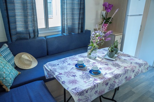 Tavolo apparecchiato con tovaglia floreale, fiori in vaso e seduta blu.