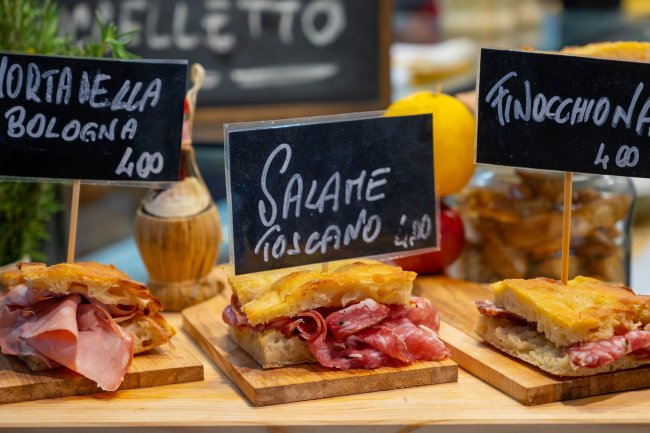 Tre panini con diversi tipi di salumi italiani esposti su un tavolo di legno.