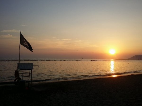 Spiaggia al tramonto con bandiera nera su un palo e mare calmo.