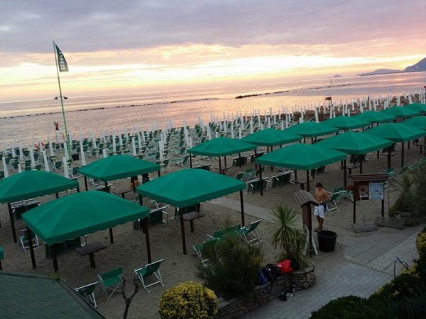 Stabilimento balneare con ombrelloni verdi e lettini sulla spiaggia al tramonto.