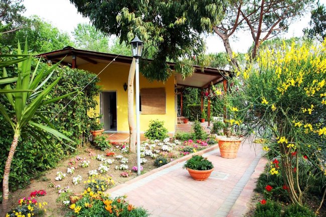 Casa gialla con giardino fiorito e sentiero in mattoni.