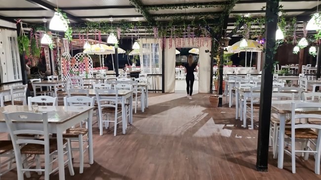 Un ristorante con tavoli e sedie bianche, decorato con piante e luci appese.