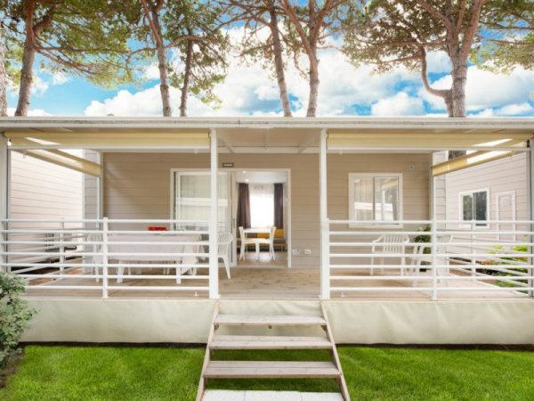Bungalow in legno con veranda, due aree relax, scale e prato verde.