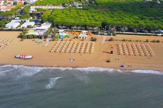 Spiaggia con ombrelloni ordinati, mare in primo piano e area verde sullo sfondo.
