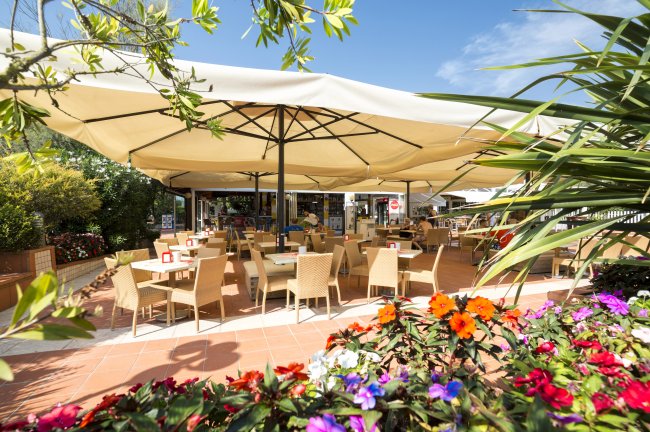 Un bar esterno con tavoli e sedie sotto grandi ombrelloni, circondato da fiori colorati.